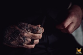   A detailed close-up at La Factory in Thizy-les-Bourgs, Rhône, France, shows the groom’s tattooed hands as he prepares in his sleek all-black suit, ready for his wedding.